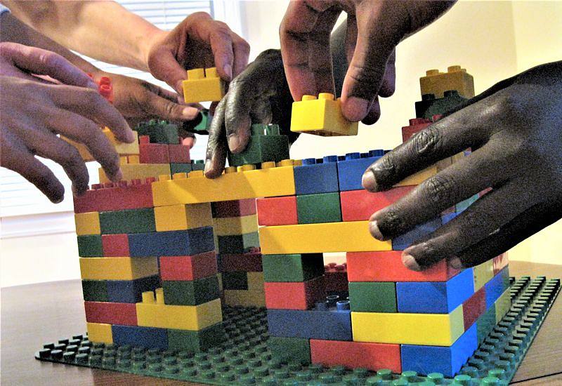 many hands working together to build house with legos