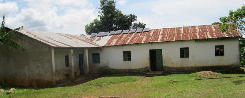 simple white cement building with nine solar panels on rusted tin roof