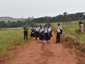 students on dirt road wearing white shirts, dark pants or skirts, and red neckties
