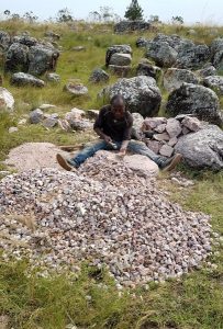 man sitting and pounding rocks, with a pile of small rock pieces in front of him