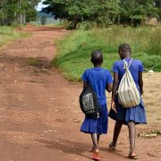 two young girls with blue uniforms and backpacks walking on a dirt road