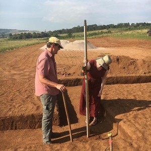 A man and young woman standing in a foundation trench and using a story pole to measure elevations
