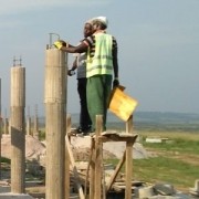 two Tanzanian men on scaffolding looking at the top of a building column