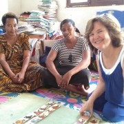 American woman and two Tanzanian women working a children's activity on the floor with many books in background