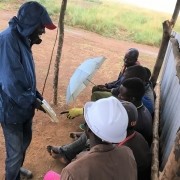 man in raincoat showing a book to construction crew sitting under shelter
