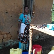 African woman in colorful dress standing in front of mud brick building