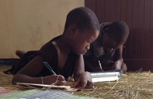 two children doing homework on a floor covered with grass