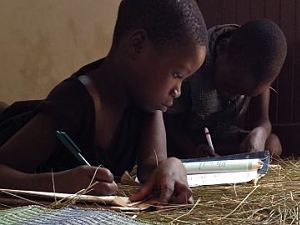 two children doing homework on a floor covered with dry grass