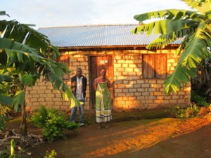 man and women in front of clay brick house with tin roof and banana trees