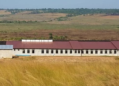 long building with dark red roof in grassy field