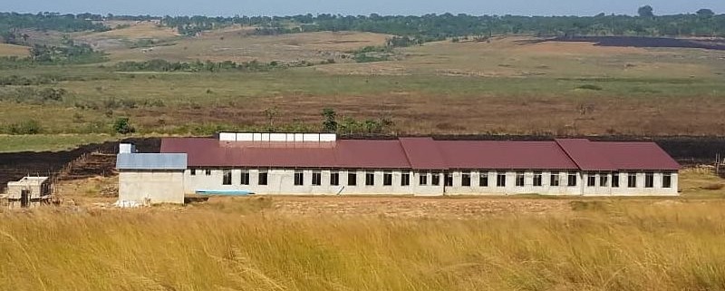 long building with dark red roof in grassy field