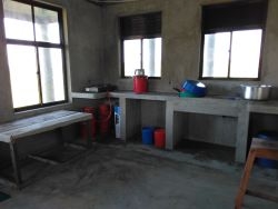 inside of a simple school kitchen with propane stove and cement counter and sink
