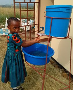child washing hands at a plastic bucket on a metal stand