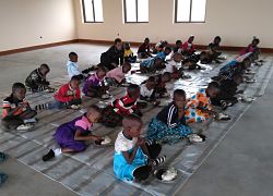 children sitting on a tarp in a large room eating from plates with their fingers