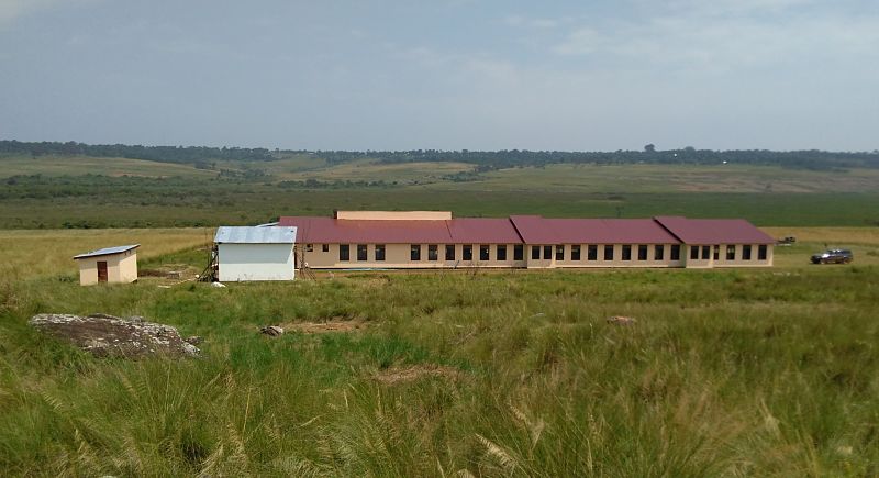 long school building with grassy field in foreground and hills in background