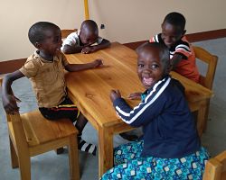 kids with big smiles sitting in small chairs at a wooden table