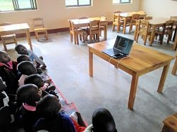 laptop on student table with kids gathered in front