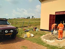 landcruiser parked next to butterscotch colored storage shed and two men in orange suits mixing cement