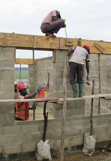 workers at cement block wall on wooden scaffold with bucket and cement trowel