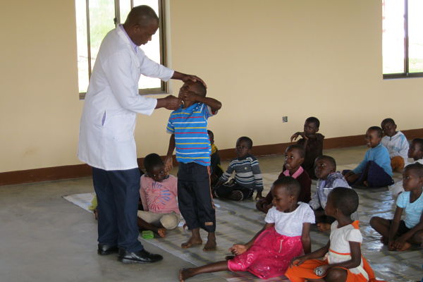 man in white lab coat inspecting a young boy's teeth in a group of children