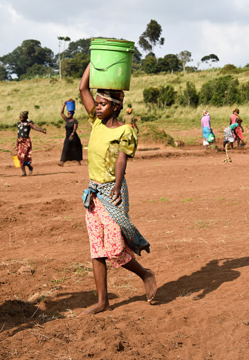 women in bright clothing carrying buckets of dirt on their heads